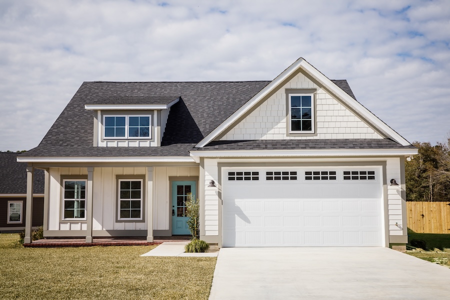 New, modern, one story house. It has a wide driveway, a garage and a small front porch.