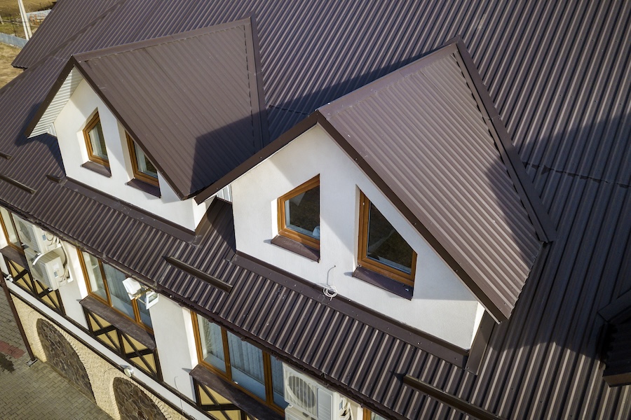 Close-up aerial view of building attic rooms exterior on metal shingle roof, stucco walls and plastic windows.