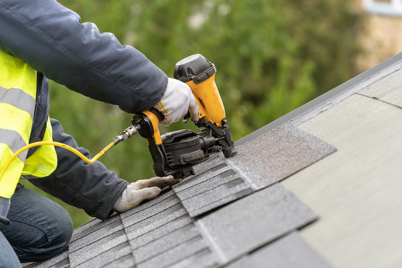 workman-using-pneumatic-nail-gun-install-tile-on-roof-of-new-house-under-construction-2