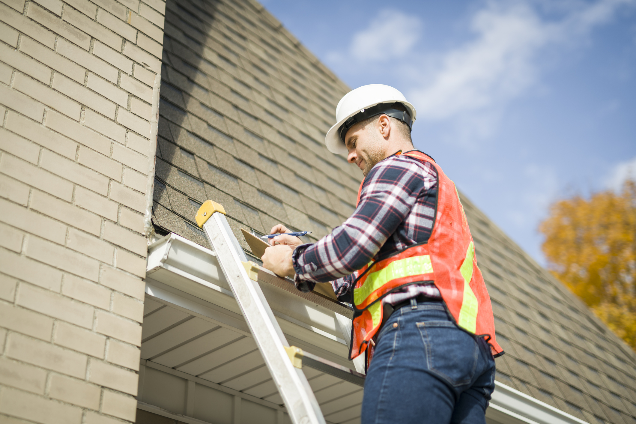 man with hard hat standing on steps inspecting house roof
